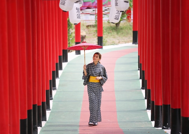 日本庭園の神社に傘をさして歩いている着物姿の女性。