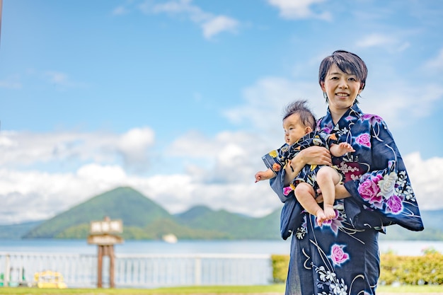 A woman in a kimono holds a baby in front of a lake