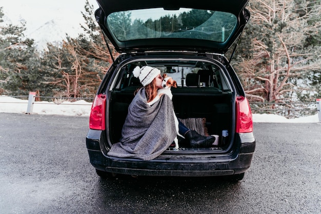 woman kissing dog while sitting in car trunk
