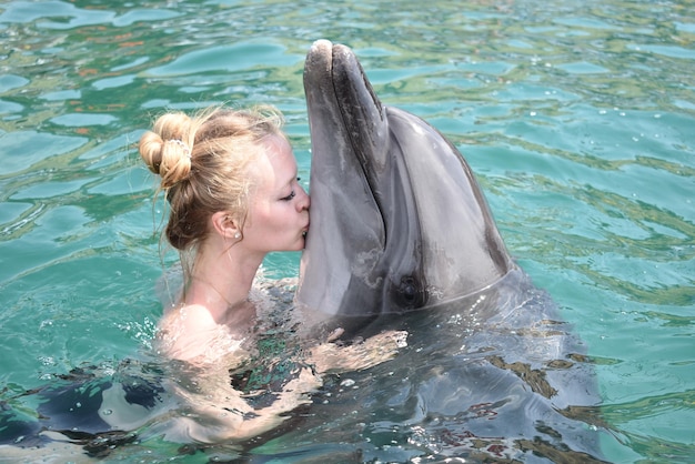 Woman kissing dolphin while swimming in pool