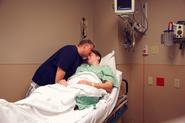 woman kissing wife on bed in hospital