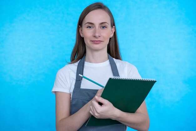 A woman in a kitchen apron writes in a notebook