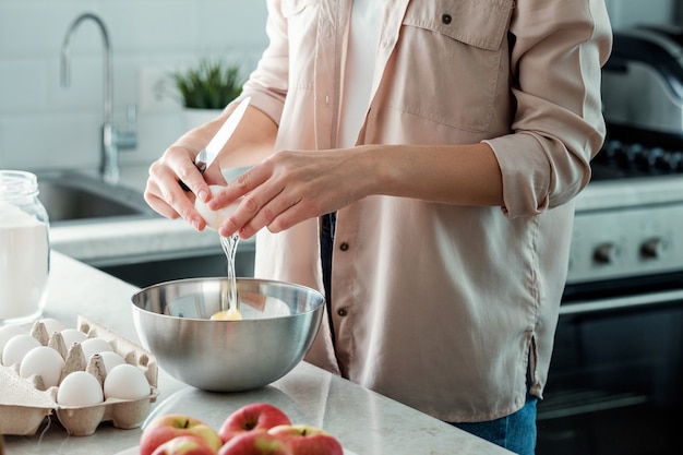 A woman in the kitchen breaks a chicken egg with a bowl. Cooking.