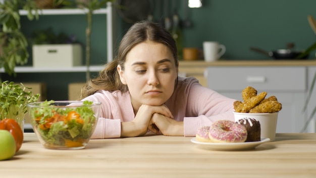 A woman in the kitchen chooses between healthy organic food and\
glazed donuts