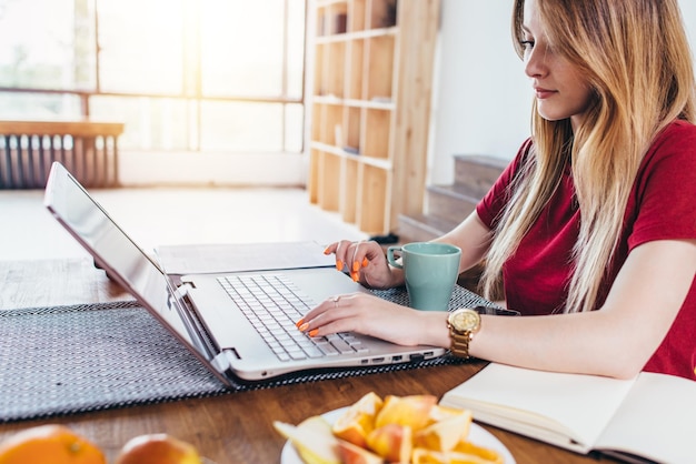 Woman in kitchen during her breakfast using her laptop