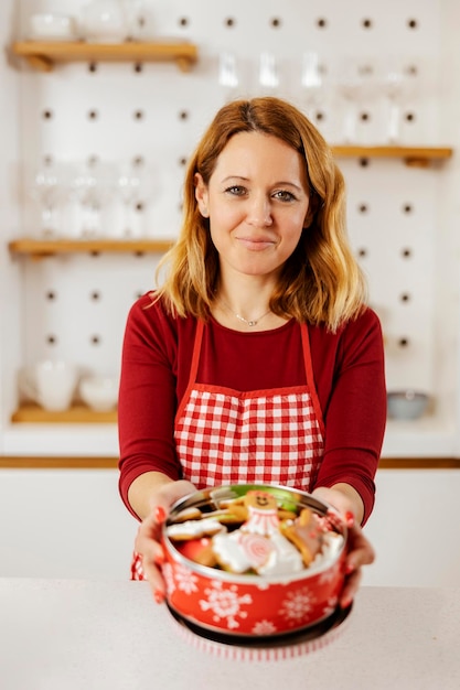 A woman in kitchen is holding a box with ginger cookies made for New Year's eve while smiling at the camera