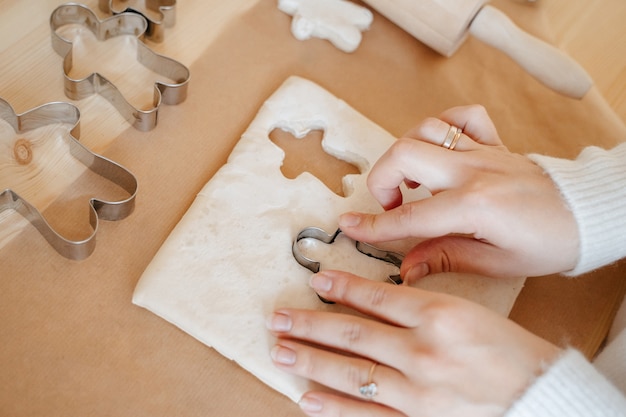 Foto la donna in cucina prepara i biscotti allo zenzero di natale usando stampi in metallo a forma di uomo. concetto di cottura per le vacanze di natale