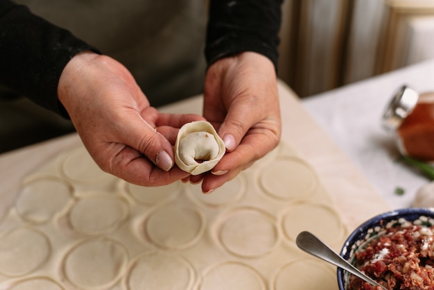 A woman in the kitchen sculpts homemade dumplings or semi-finished products. The cook wraps the minced meat from beef into the dough