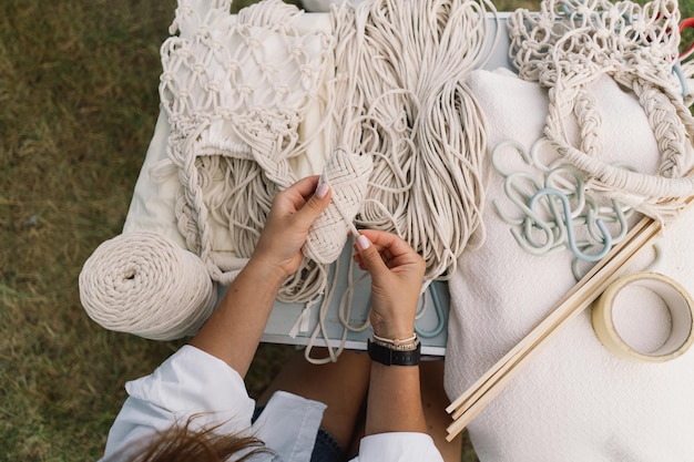 Woman knits bag using macrame technique outdoors near tents Outdoor hobbies Macrame weaving