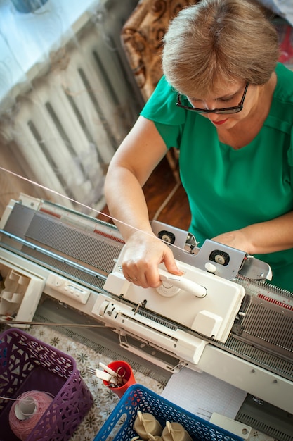 Woman knits on a knitting machine, working with her hands