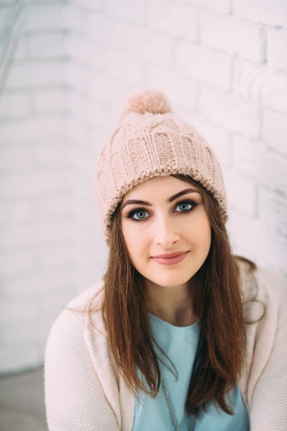 Woman in knitted hat sitting near a brick wall