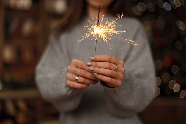 Woman in knitted sweater celebrates the holiday with amazing sparklers in female hands. close-up.