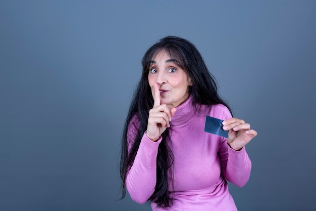 Woman in knitted sweater holding card on black and showing secret gesture isolated gray