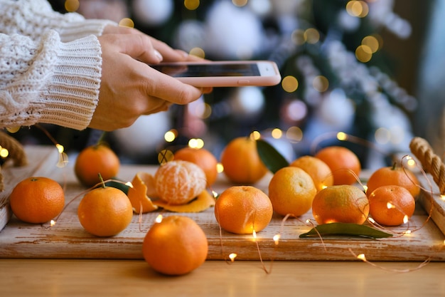 Woman in knitted sweater makes a photo on smartphone of Christmas composition