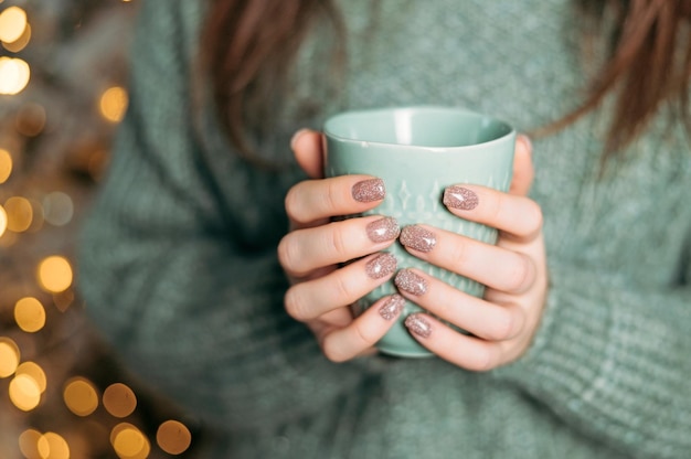 Woman in knitted wool sweater is holding a mug with hot chocolate or coffee cozy holiday atmosphere