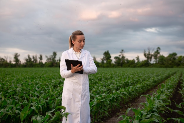 A woman in a lab coat stands in a field with a pad in front of her.