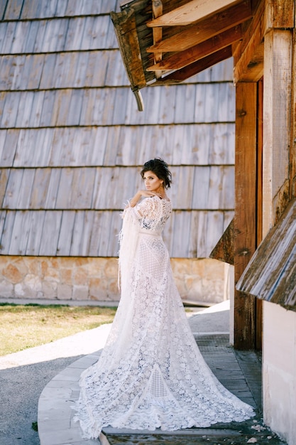 Woman in a lace dress stands by an old hut