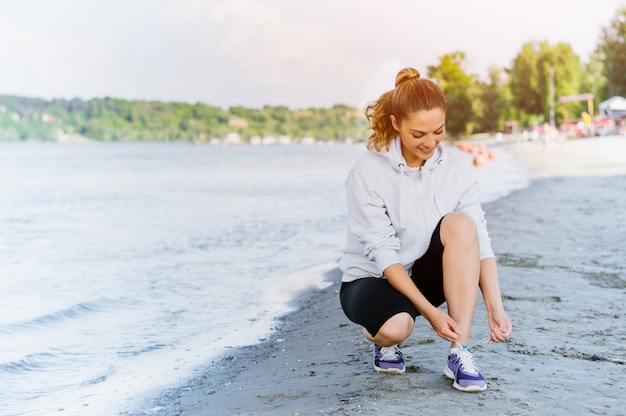 Woman lacing sport shoes and getting ready for running and exercising at beach on summer