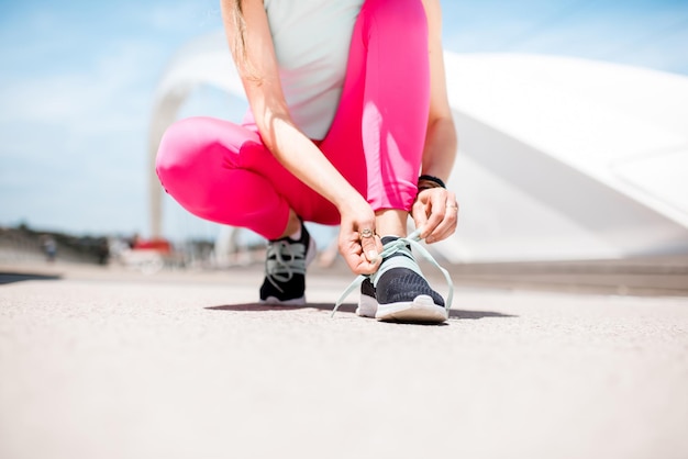 Woman lacing up a sports sneakers standing outdoors on the white bridge