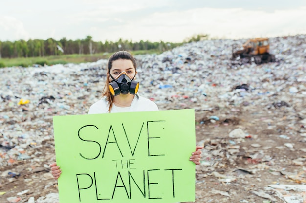 Foto donna in una discarica volontaria con in mano un poster per salvare la terra