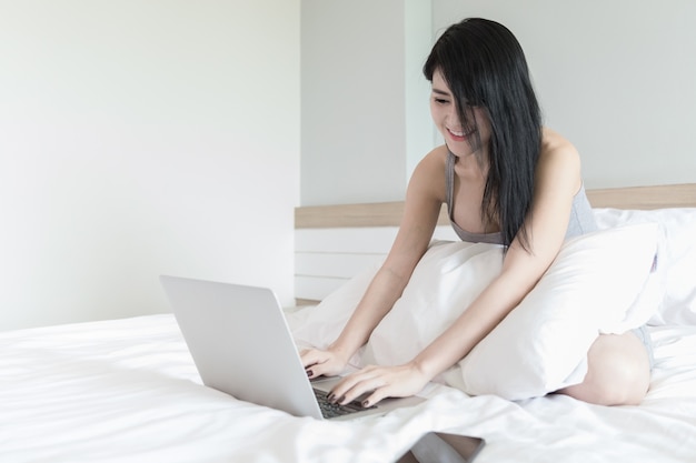 woman and laptop in bedroom on white bed