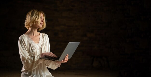 Woman and laptop in an empty dark room Deadline a lot of work privacy Middle age woman in a white shirt Banner place for text