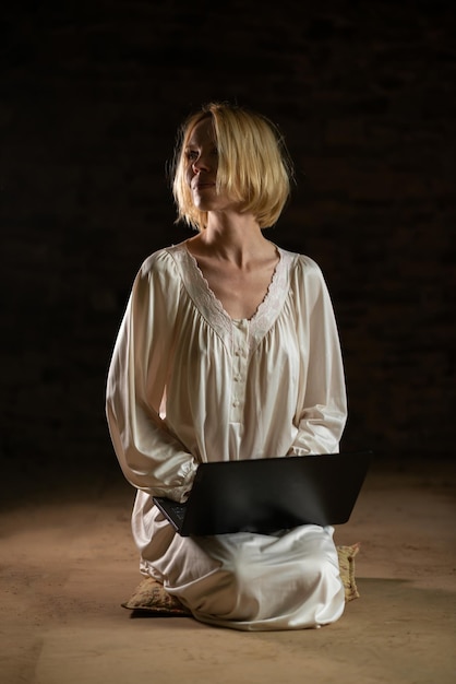 Woman and laptop in an empty dark room Middle age woman in a white shirt