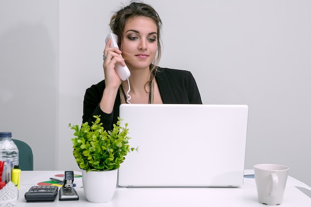 Woman at laptop talking phone in office