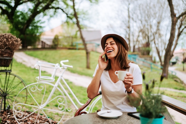 Женщина смеется во время разговора по телефону в кафе.