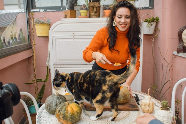 ソーシャル ネットワーク用に食べ物のビデオを作成しているときにテーブルに猫を乗せて笑っている女性の邪魔をする