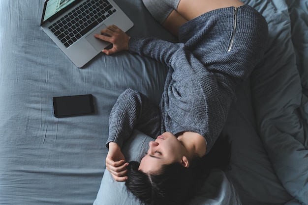 Woman lay on bed with gray sheets in gray clothes. watch movie on laptop in bed. overhead view