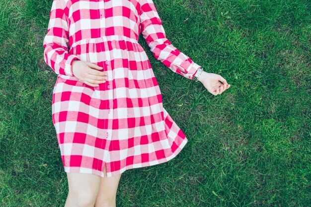 Woman lay on green grass in red dress overhead view