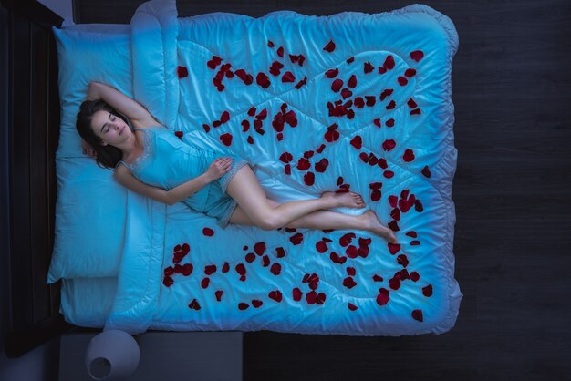 The woman laying on a bed with rose petals. evening night time, view from above