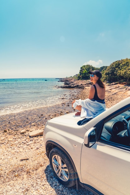 海の夏のビーチの景色を望む車のフードに横たわっている女性