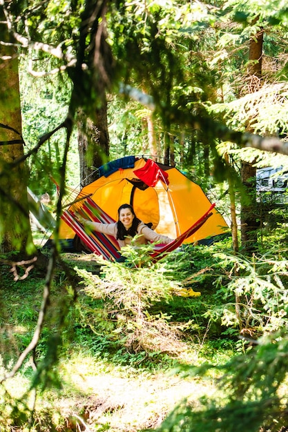 背景の森のテントのハンモックで横になっている女性