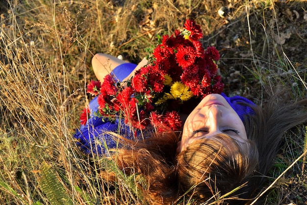 A woman laying in the grass with a bunch of flowers in her hand.