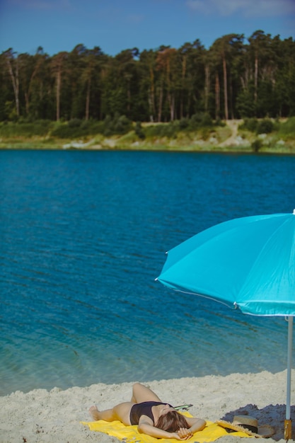 Woman laying on yellow blanket at sand beach with blue sun umbrella