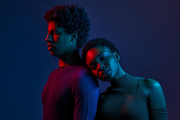 Woman leaned on man shoulder, young confident people in neon light over dark studio background