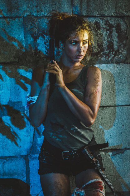 Photo a woman leaning against a wall with a gun