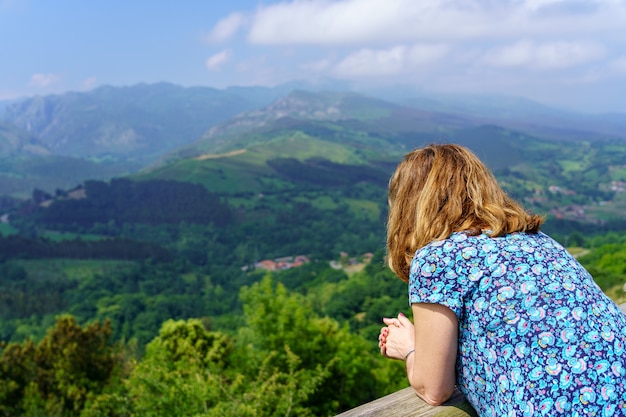 Woman leaning out of a viewpoint contemplating the green landscape of the valley