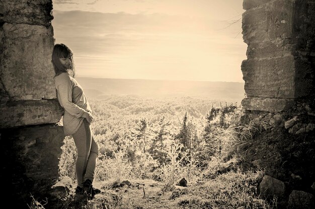 Photo woman leaning on wall against landscape during sunset