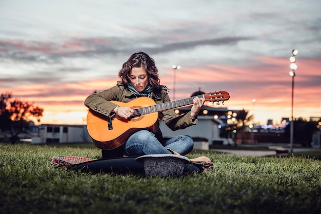 Woman learns to play guitar in a park at dusk