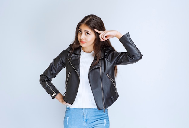 woman in leather jacket pointing at head and thinking.