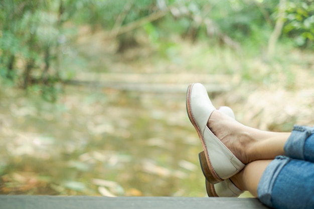 Gamba e scarpa della donna che si siedono sul pilastro di legno