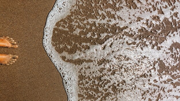 woman legs barefoot at sea foam waves on sand beach summer day. top view above women feet