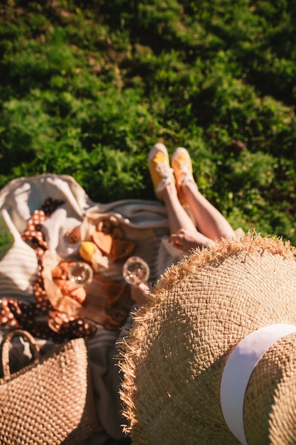 Gambe della donna sulla coperta che hanno picnic sul cibo del tramonto bevanda all'aperto estate