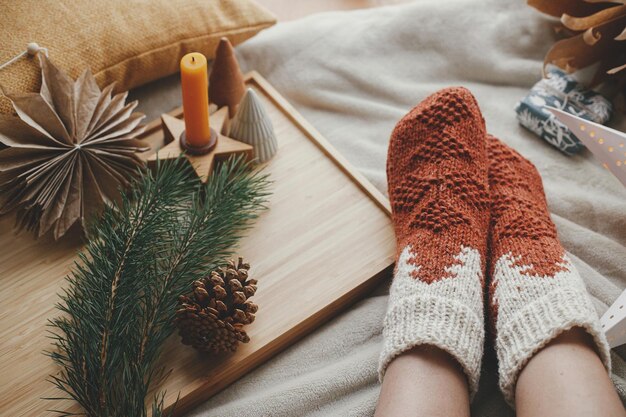 Woman legs in warm socks on soft blanket with christmas star\
trees candle cozy home winter hygge