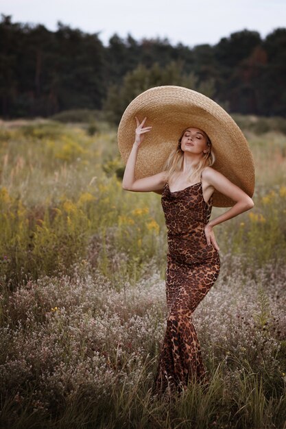 Woman in leopard dress and straw hat in summer meadow