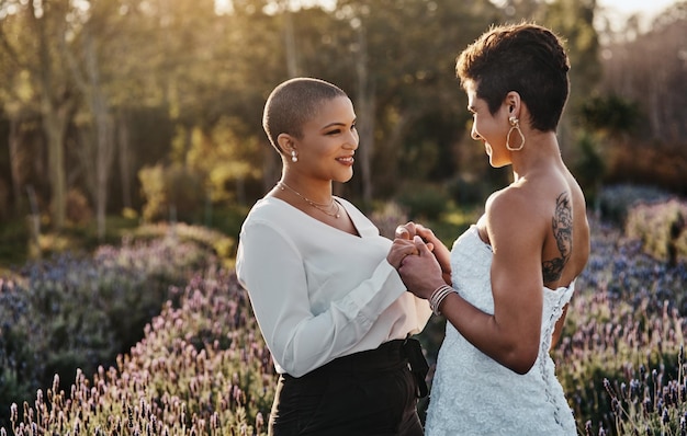 Photo woman lesbian couple and holding hands in marriage for wedding with smile for lgbt relationship in nature happy gay married women touching hand and smiling for romance vow or loyalty outside