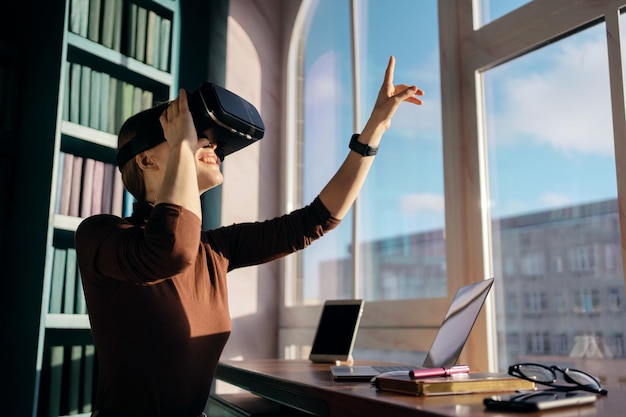 A woman in a library wearing a vr headset and looking out a window.